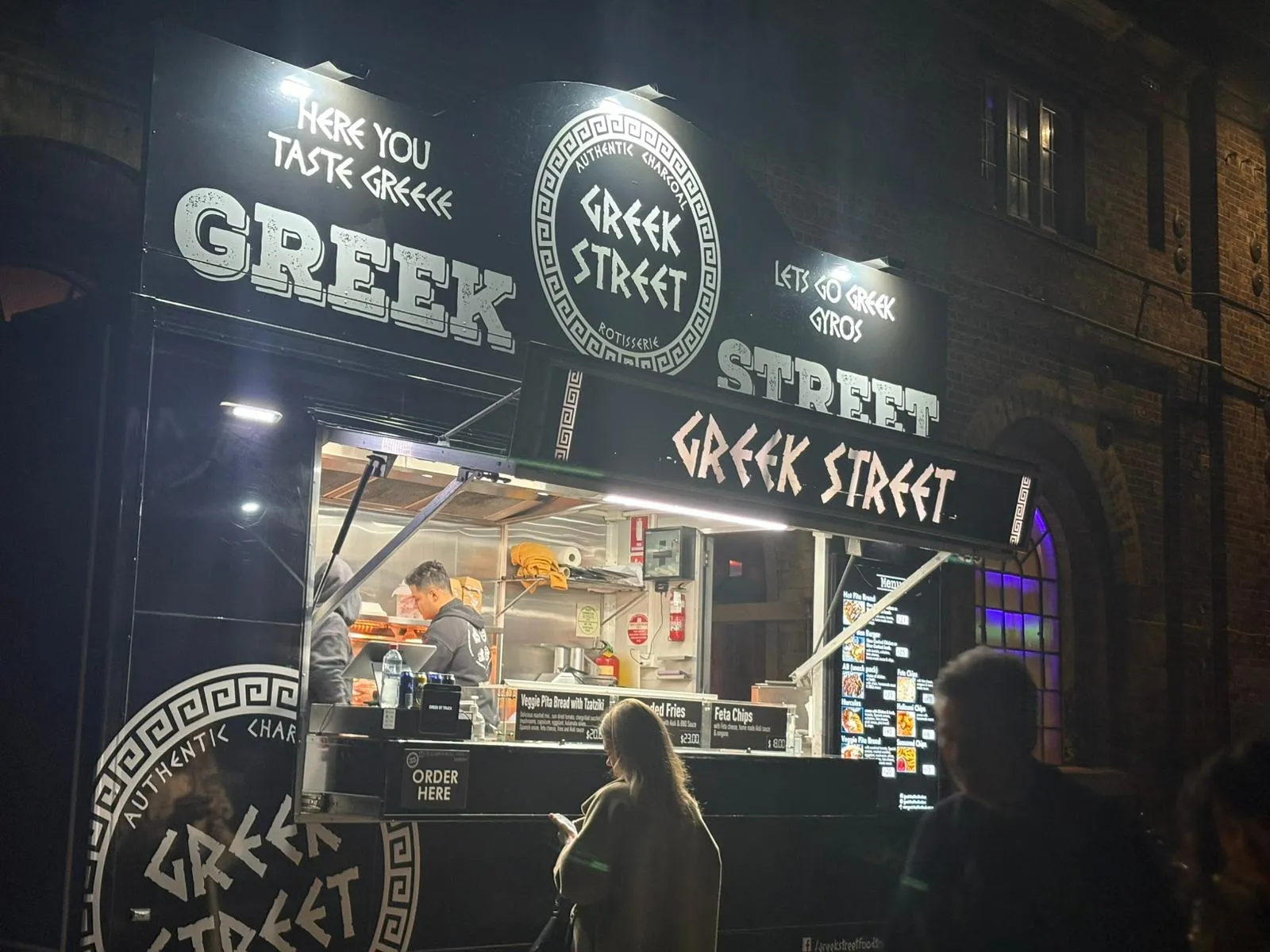 The Greek Street truck lit up at night with a customer ordering at the window