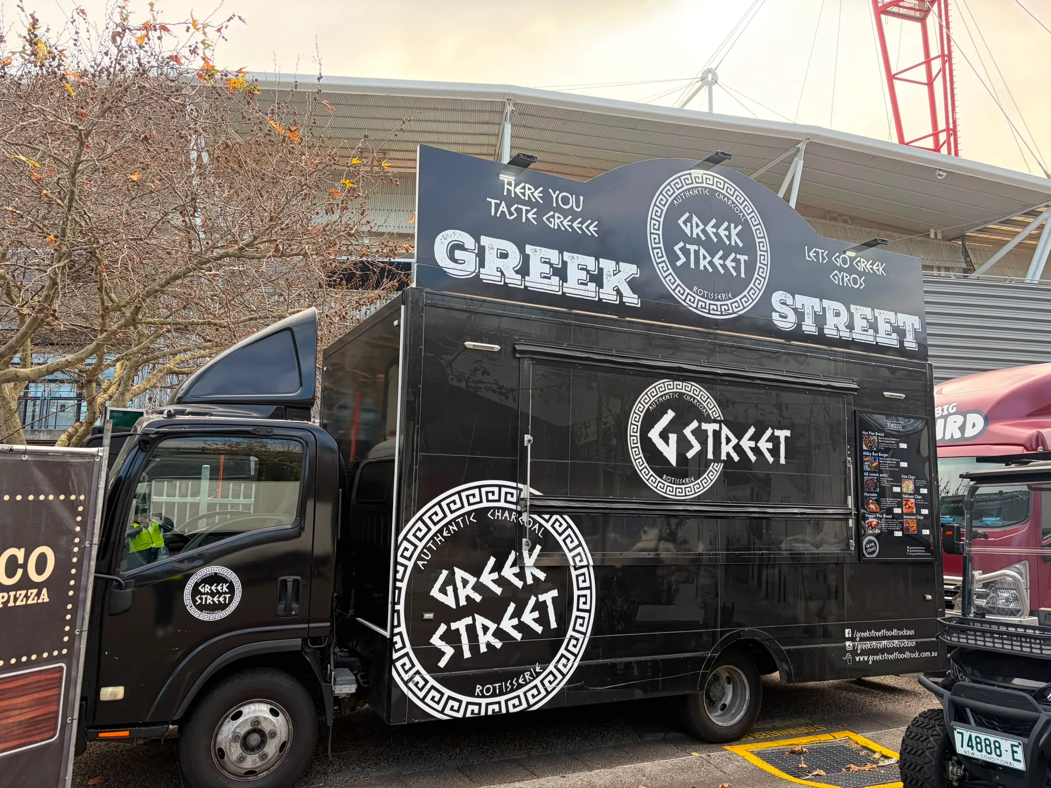 The black Greek Street food truck parked outside a stadium
