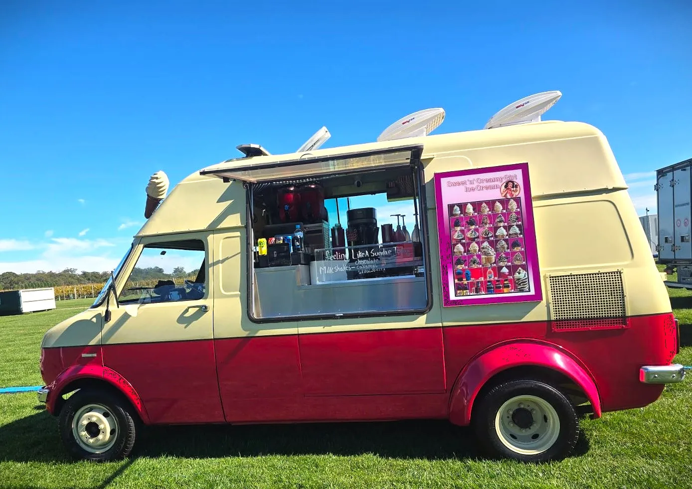 The cream and red Sweet & Creamy ice cream van parked on grass at an event